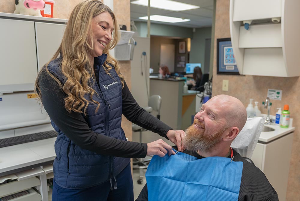 dental assistant helps a patient put on a bib